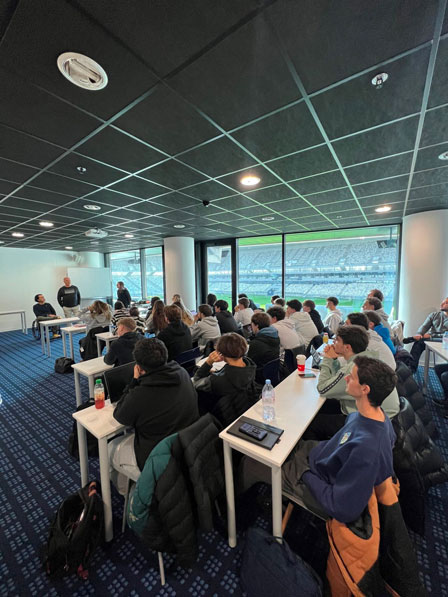 classe d'étudiants écoutant une conférence dans une salle, à côté d'un stade de sport
