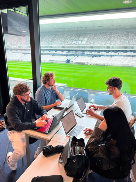 4 étudiants travaillants sur leur ordinateur à côté d'un stade