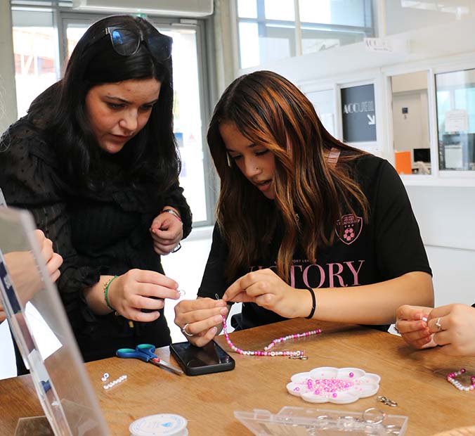 2 filles sont en train de s'aider pour faire un bracelet