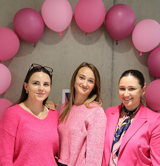 3 filles sont habillés en rose et pose devant une arche de ballon rose qui est fixé sur un mur