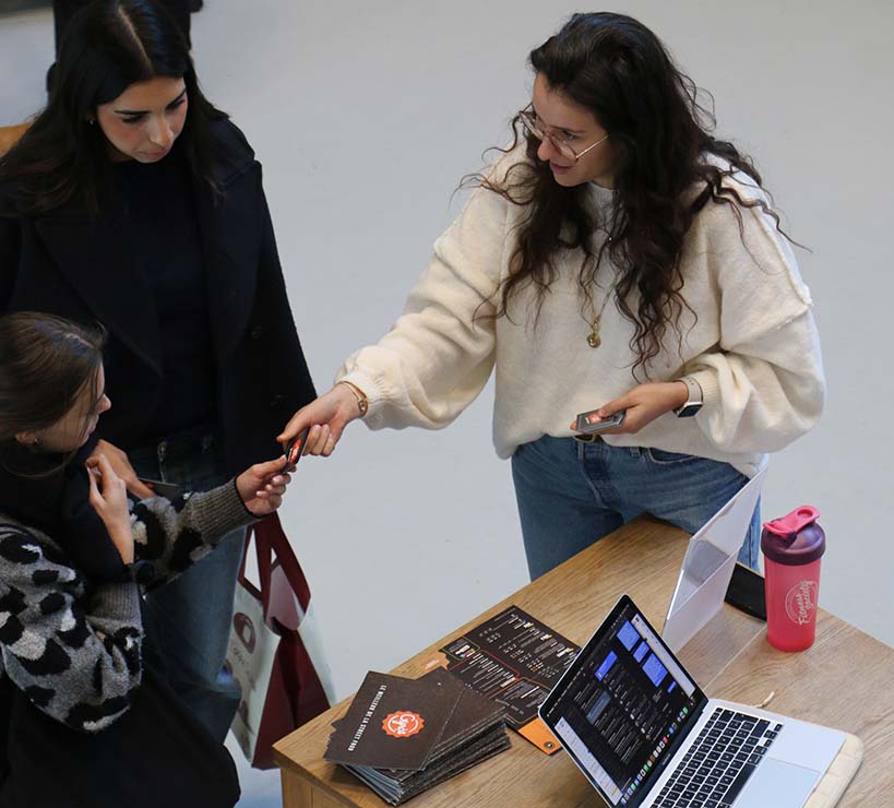 une dame distribue des coupons de réductions à deux étudiantes.