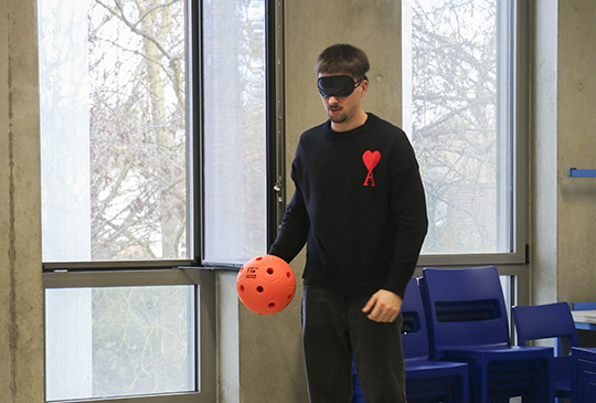 Garçon debout avec un bandeau sur les yeux et un ballon orange dans une main.