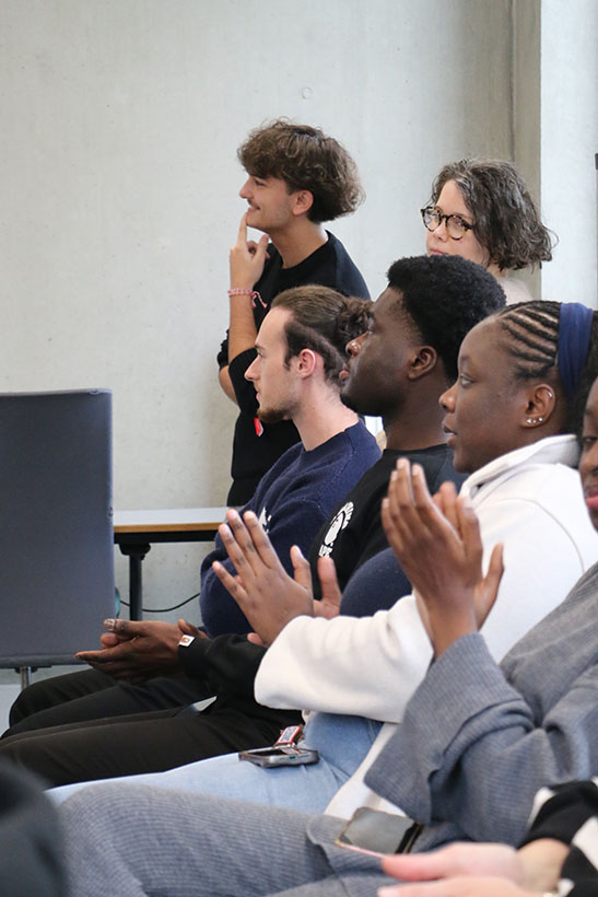 Des étudiants assis qui applaudissent en regardant devant eux.